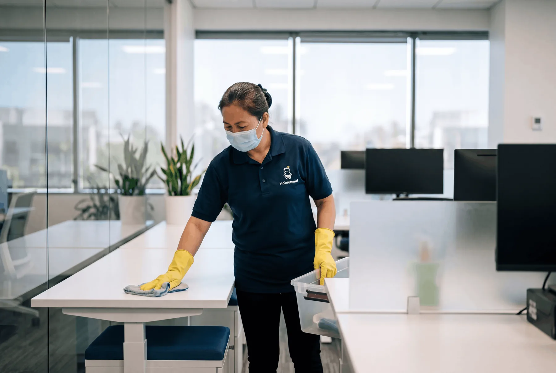 A Noblemaid cleaner wiping down desks in an open-plan office
